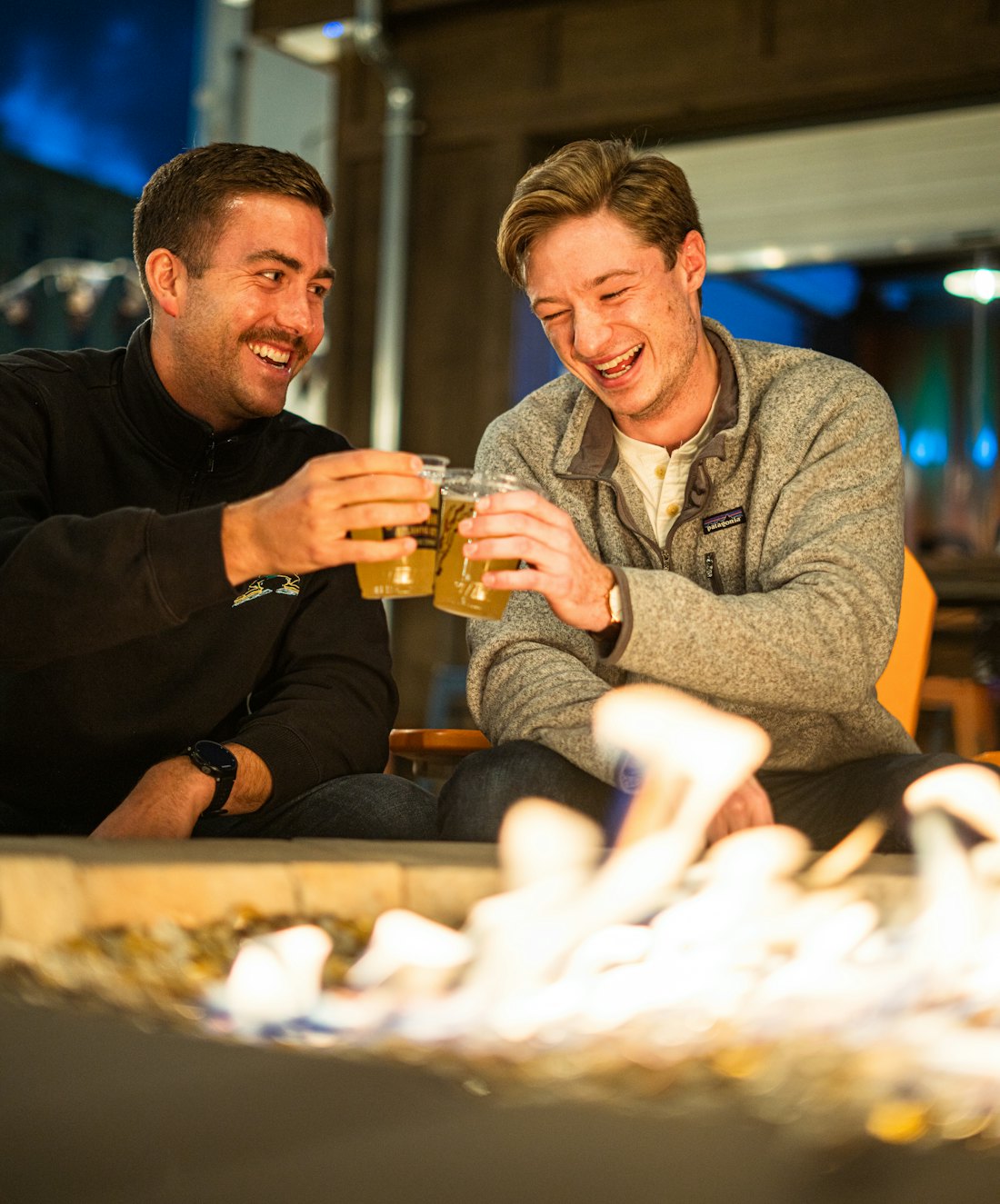 Two people laughing together over a drink outdoors in the evening